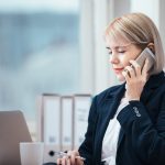 Female lawyer talking on her cell phone & working at a desk: it is always best to contact a personal injury lawyer as soon as possible after an injury
