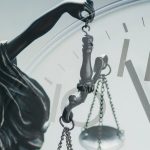 Silver statuette of Justice holding the scales of justice and law enforcement in front of a clock dial in a close up conceptual composite image