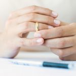 Hands of caucasian female who is about to taking off her wedding ring. Divorce papers are in front of her waiting to be signed. | Family Mediation