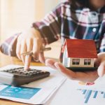 Person calculating with a model home in their hand to reference mortgage