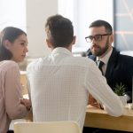 Two people talking to a man in a suit at his desk