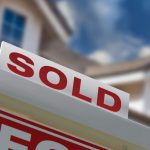 A photo of a sold sign in front of a two-story home. There is a blue sky with clouds in the background.